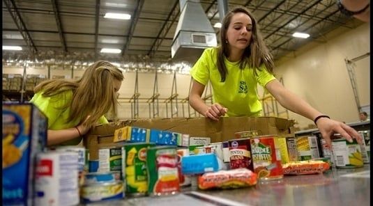 Volunteers in bright shirts sort canned food on a warehouse table