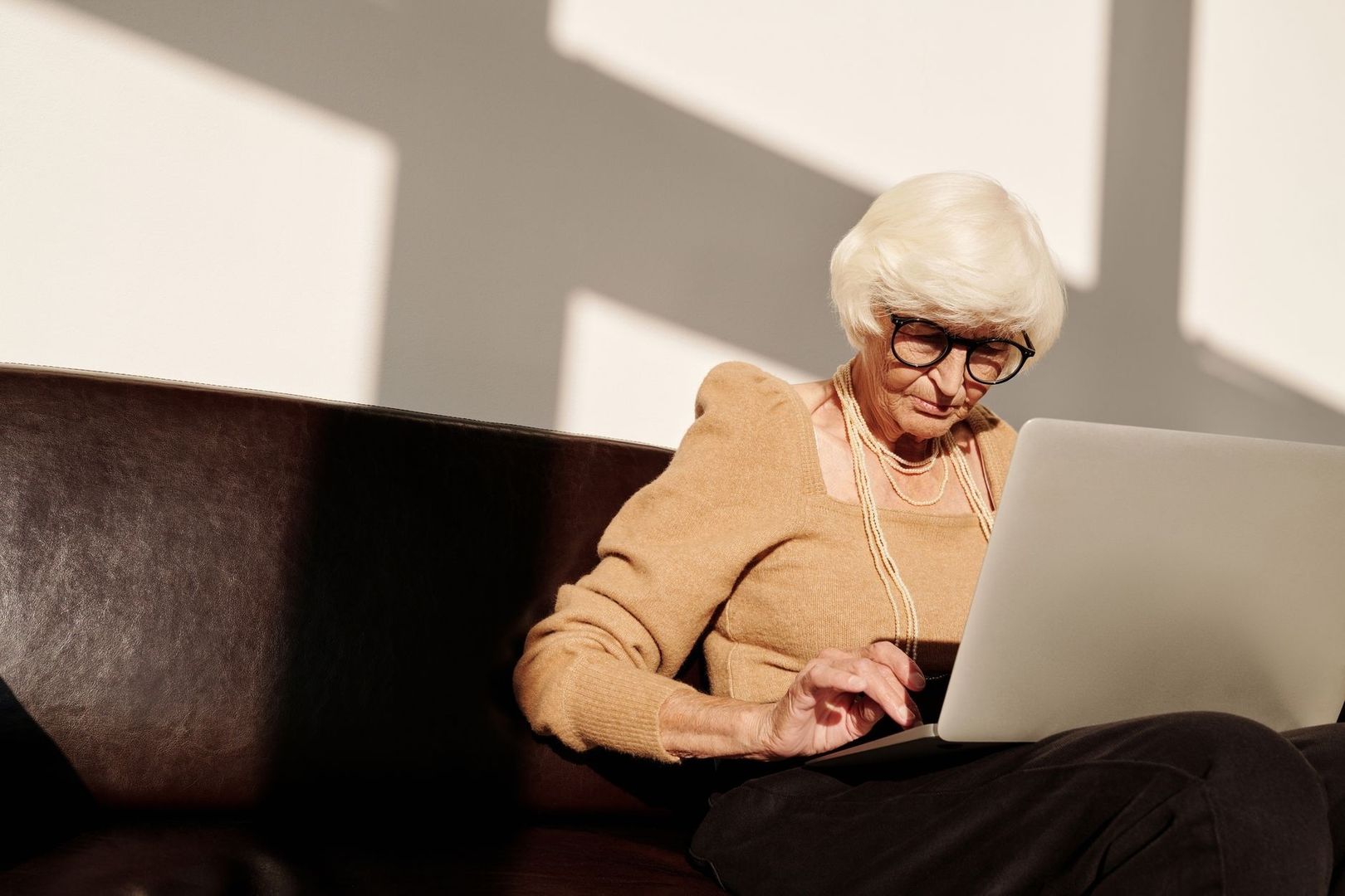 Older woman calmly typing on a laptop while seated on a sofa